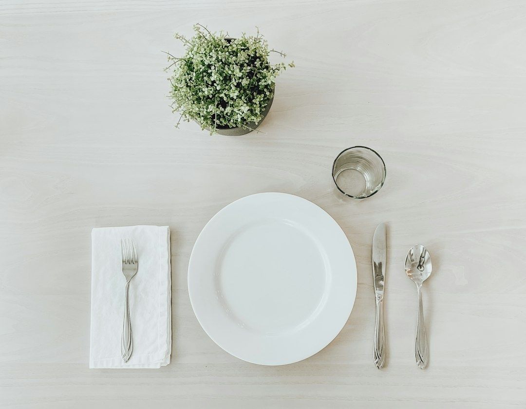 Assiette blanche et couverts disposés sur une table claire